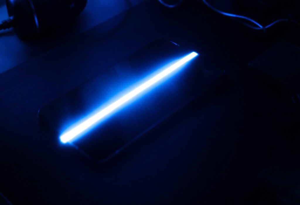 Smartphone sur un bureau sombre avec un effet de flash d'ecran, lumiere bleue